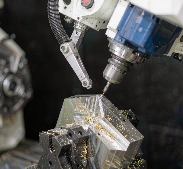 Five-axis CNC machining centre cutting a complex angled aluminium component on a trunnion table
