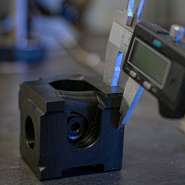 Black anodized aluminium robotics joint housing being measured with a digital caliper on an inspection bench