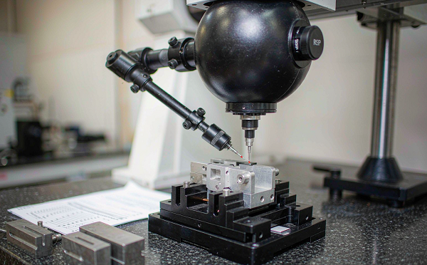 Coordinate measuring machine probe touching an aluminium part on a granite inspection table with gauge blocks nearby