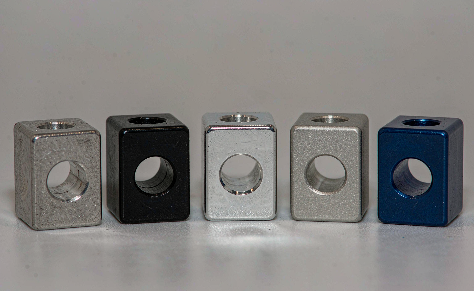Five 6061 aluminium sample blocks showing natural machined, black anodized, clear anodized, bead blasted and blue anodized finishes side by side