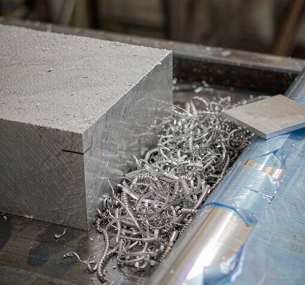 6061 aluminium raw stock including a sawn billet block, a plate with protective film partly removed and freshly machined aluminium chips