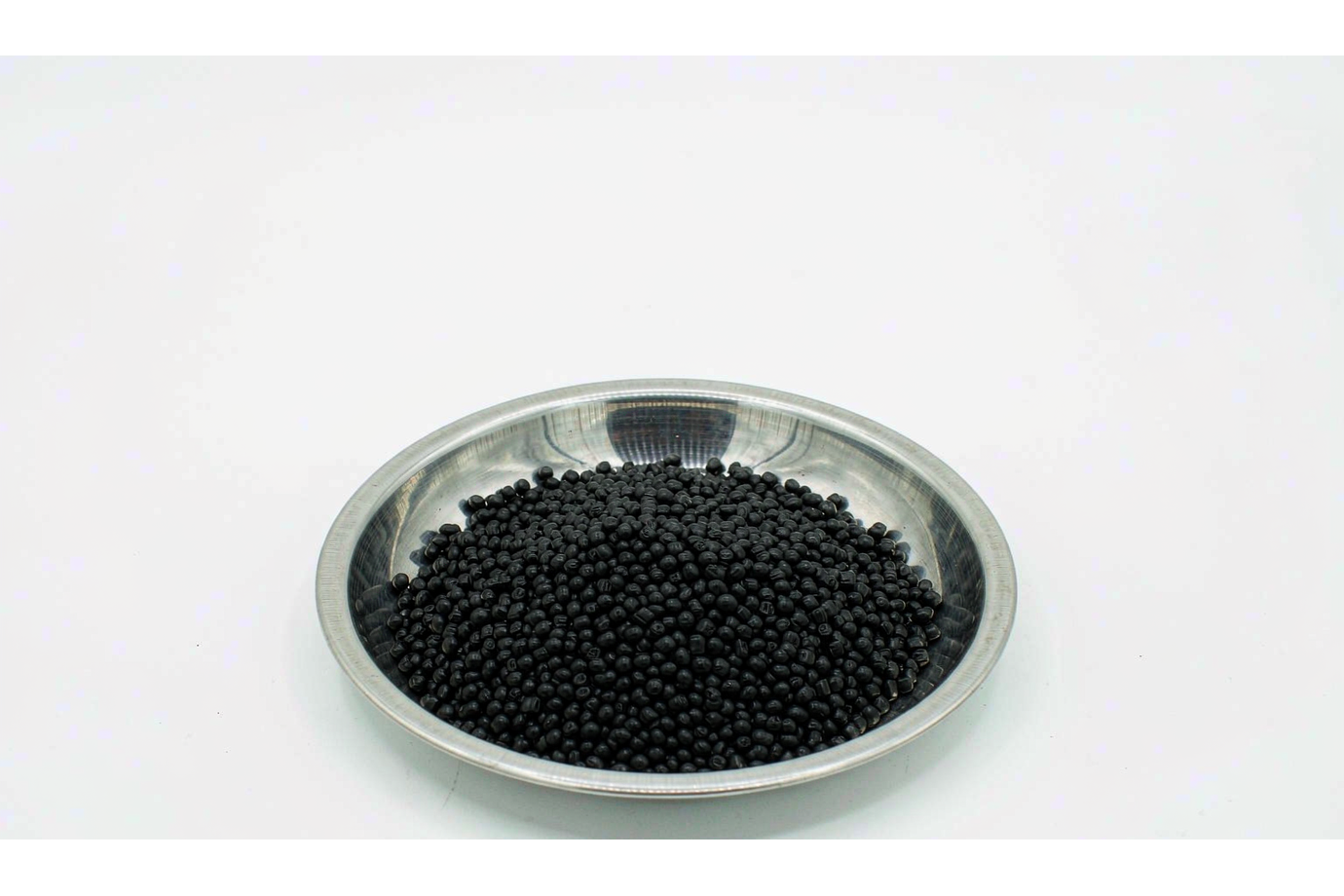 Black flame-retardant ABS pellets in a stainless steel tray on a white background