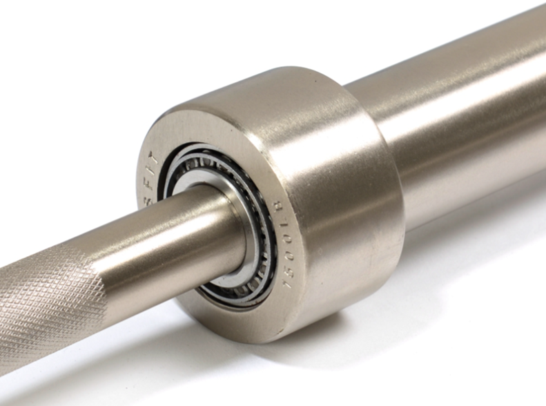 A single long precision-machined alloy steel shaft with multiple diameters and a polished bearing seat resting across a wood shipping crate