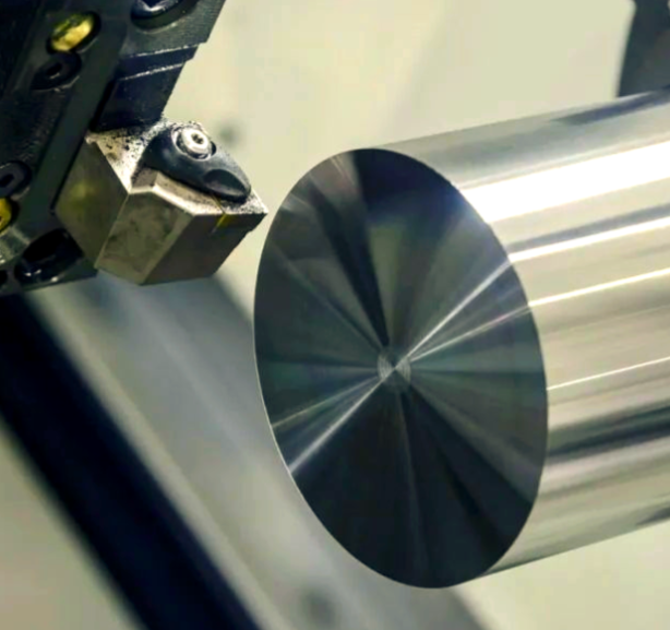 A vertical CNC machining centre milling a rectangular alloy steel block, with metal chips and coolant visible around the cutting area