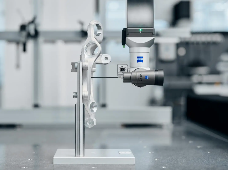 A coordinate measuring machine probing a heavy alloy steel flange part on a precision granite table with gauge blocks and a portable hardness tester nearby