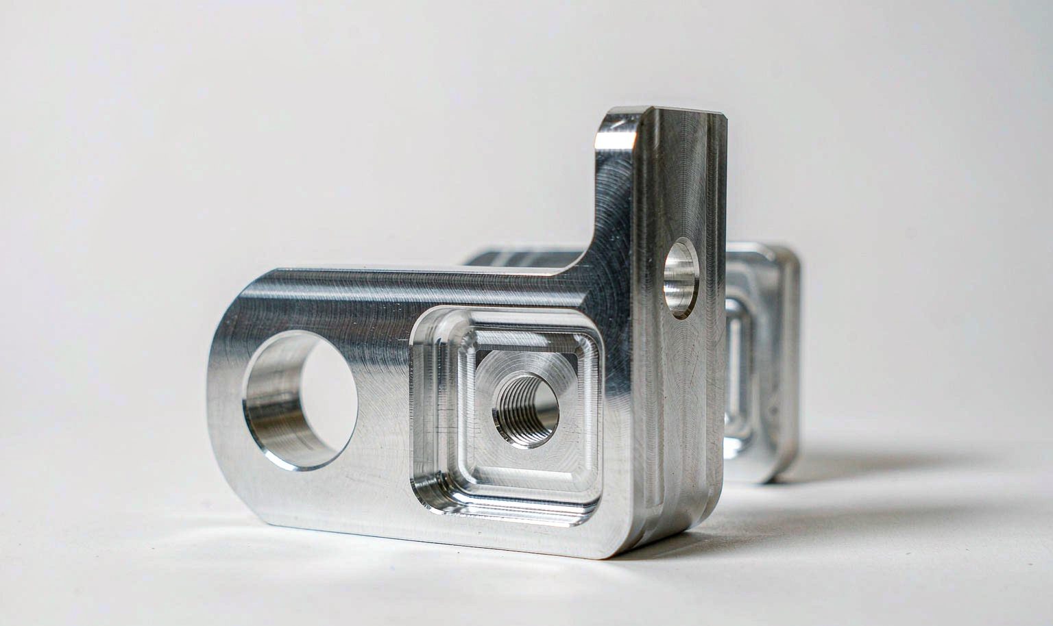 Machined aluminum bracket with milled pockets and drilled holes on a workbench