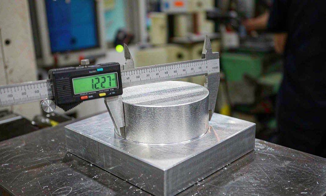 Digital caliper measuring a machined aluminum part during first-article inspection