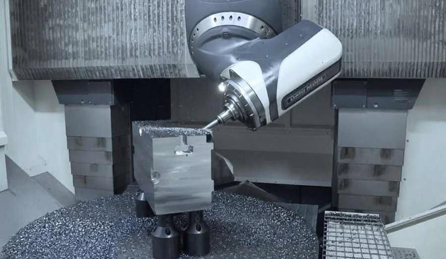 Five-axis CNC machine spindle machining a metal cube in a vise