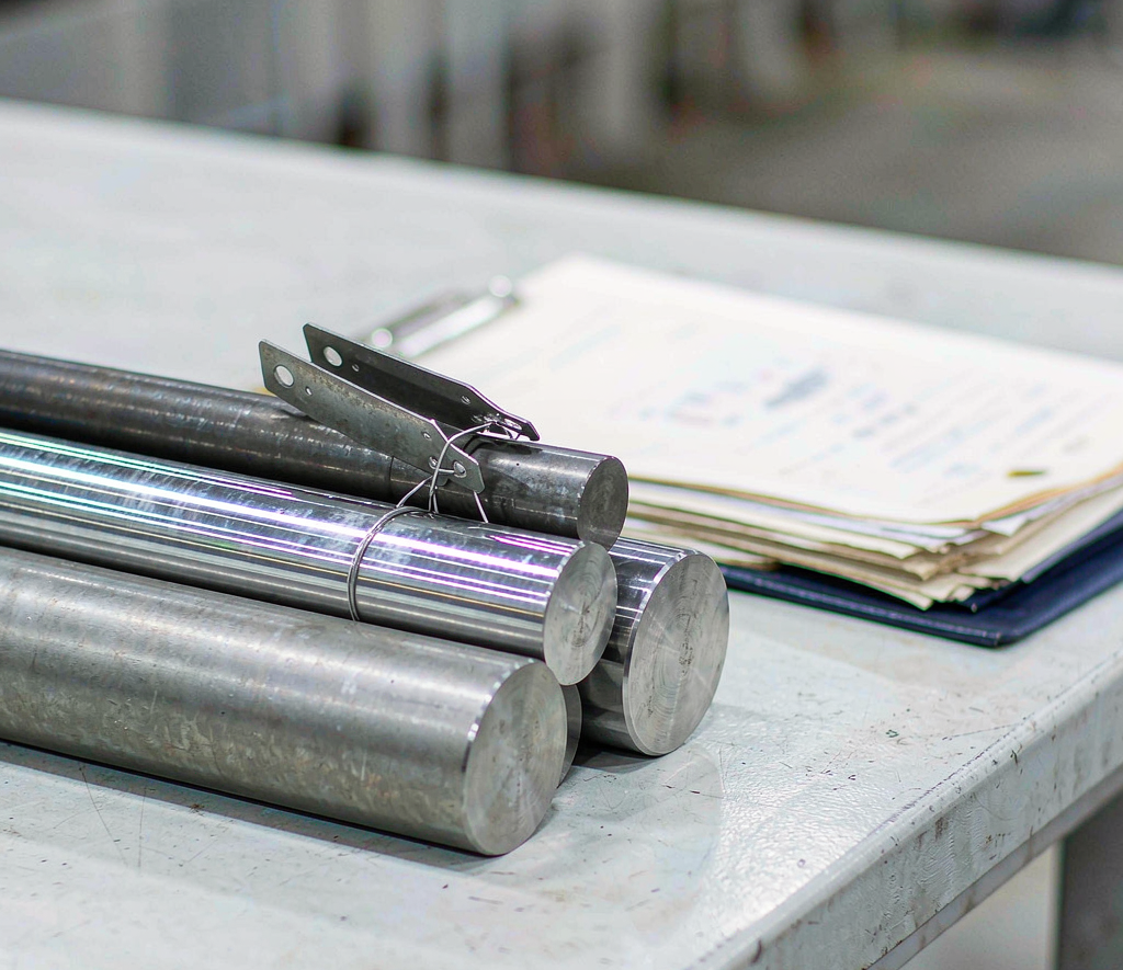 Titanium and stainless bar stock with material certificates on a clean table