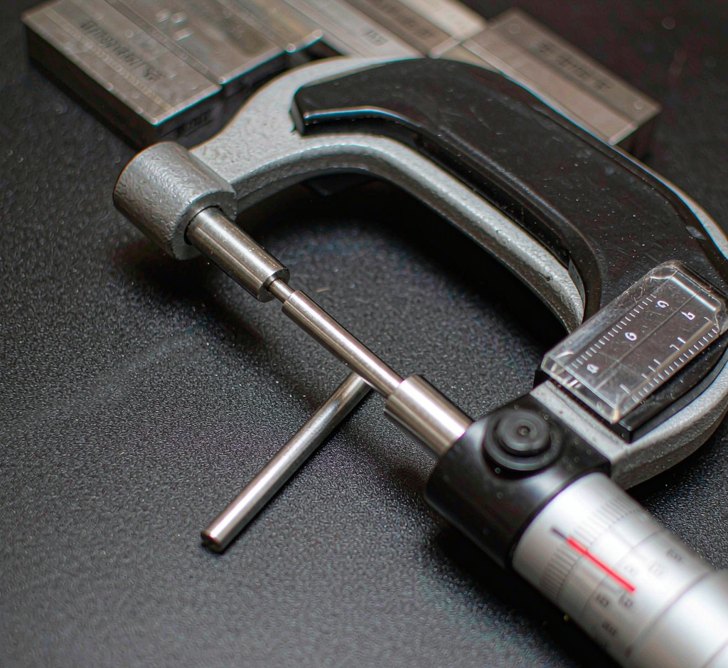 Digital micrometer measuring a precision-machined medical pin on an inspection bench