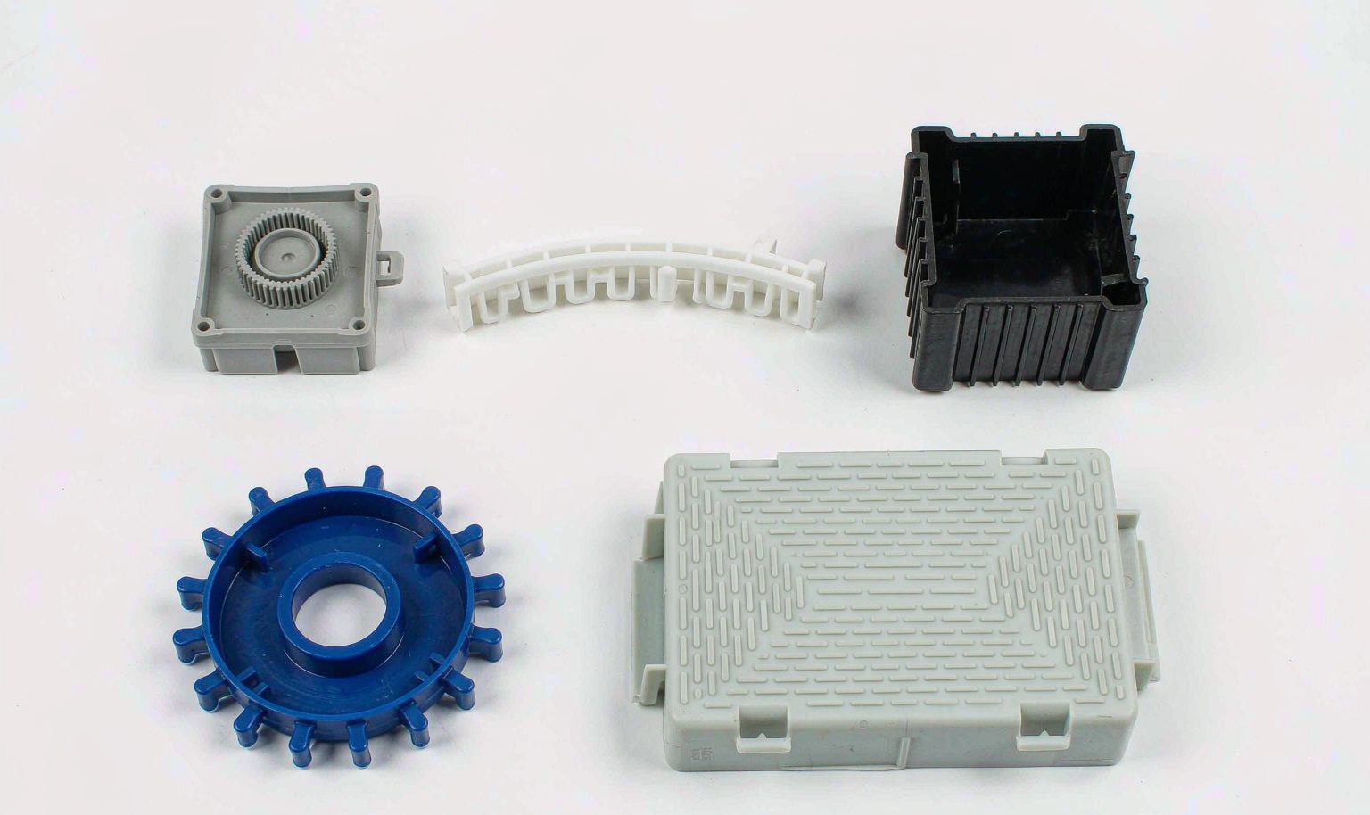Assorted custom polypropylene injection molded parts including a gear, enclosure, clip strip, and ribbed housing