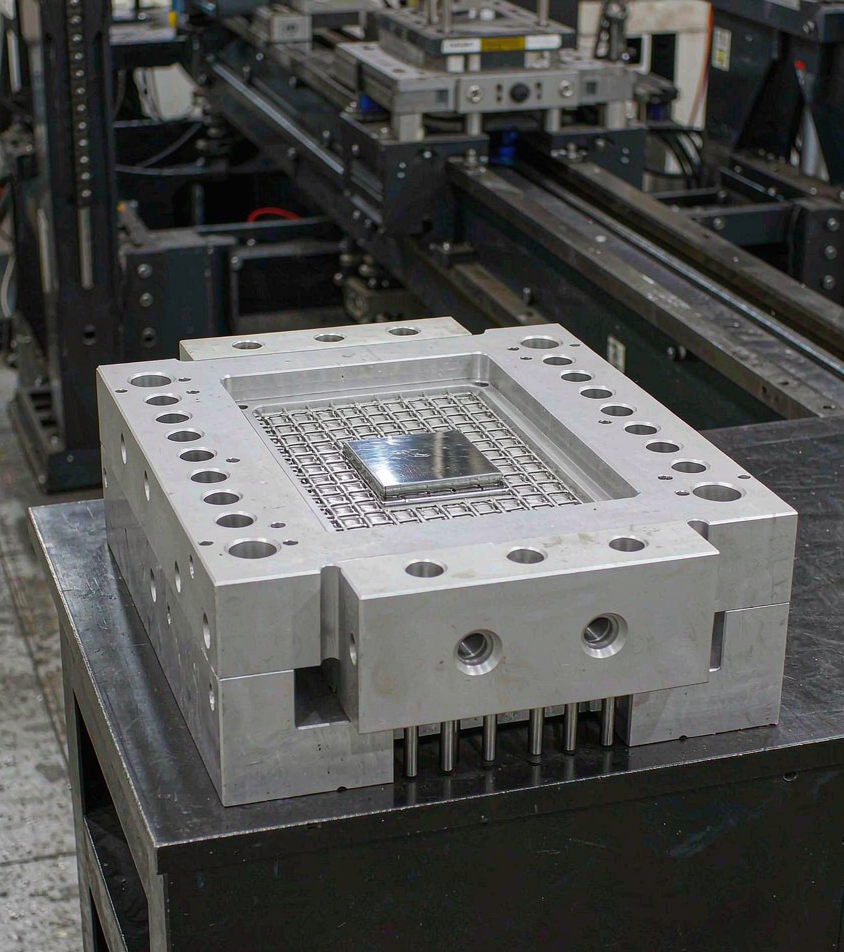 Close view of an aluminum rapid tooling injection mold block on a worktable showing machined cavities, polished steel inserts and ejector pins
