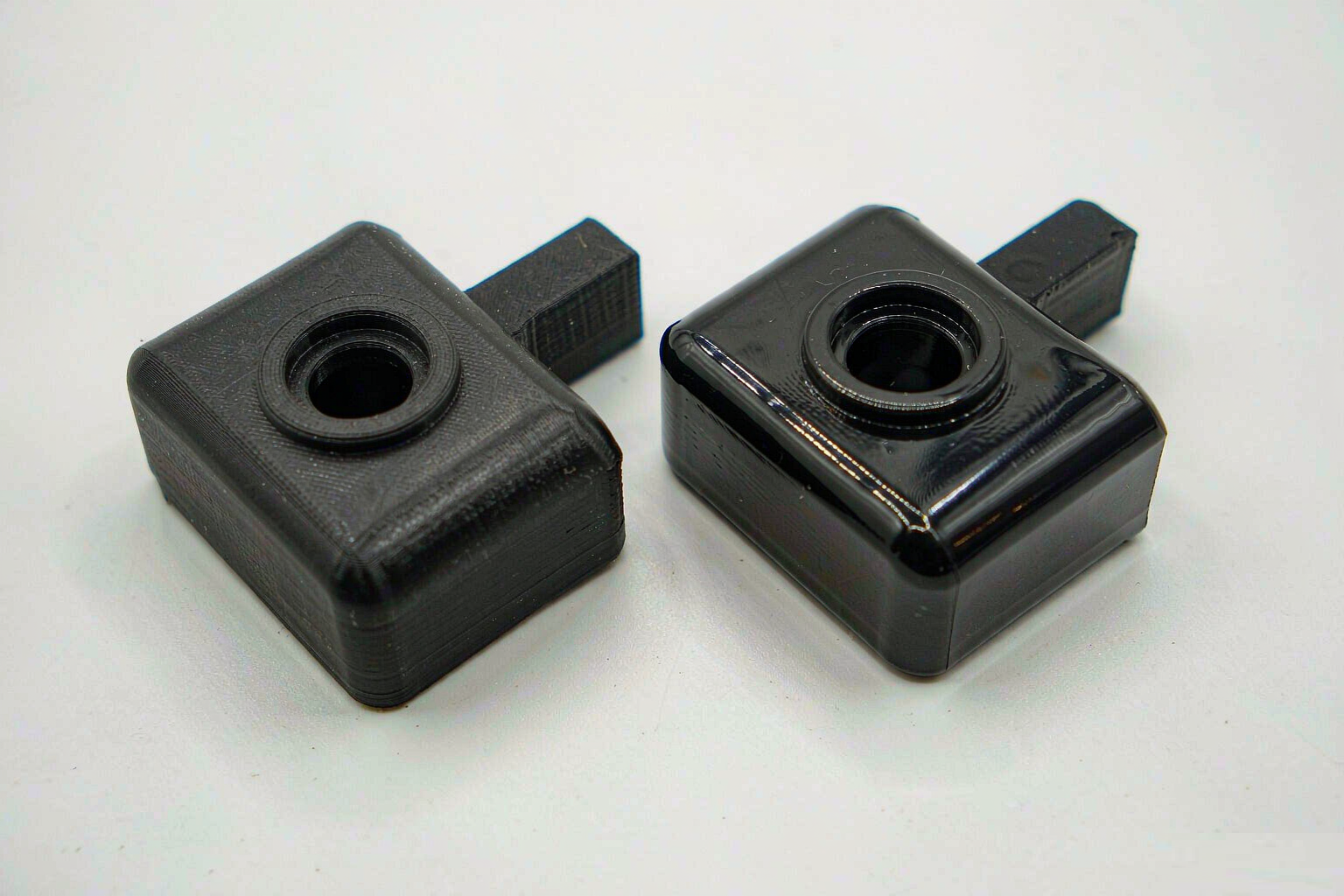 A 3D-printed plastic bracket placed beside an identical injection-molded bracket on a white background