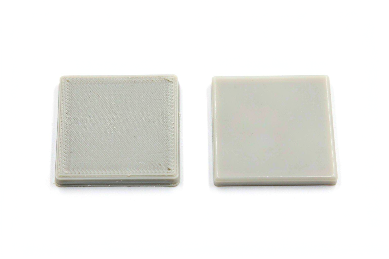 A 3D-printed plastic plaque with layer lines beside a smooth injection-molded plaque