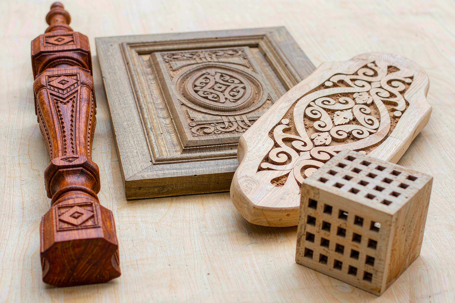 Finished CNC machined wooden components including a furniture leg, routed cabinet door panel, carved sign board and architectural model block