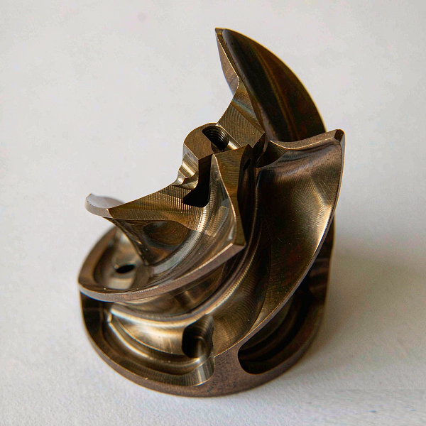 Complex multi-axis machined impeller-style metal component with curved vanes on a white surface