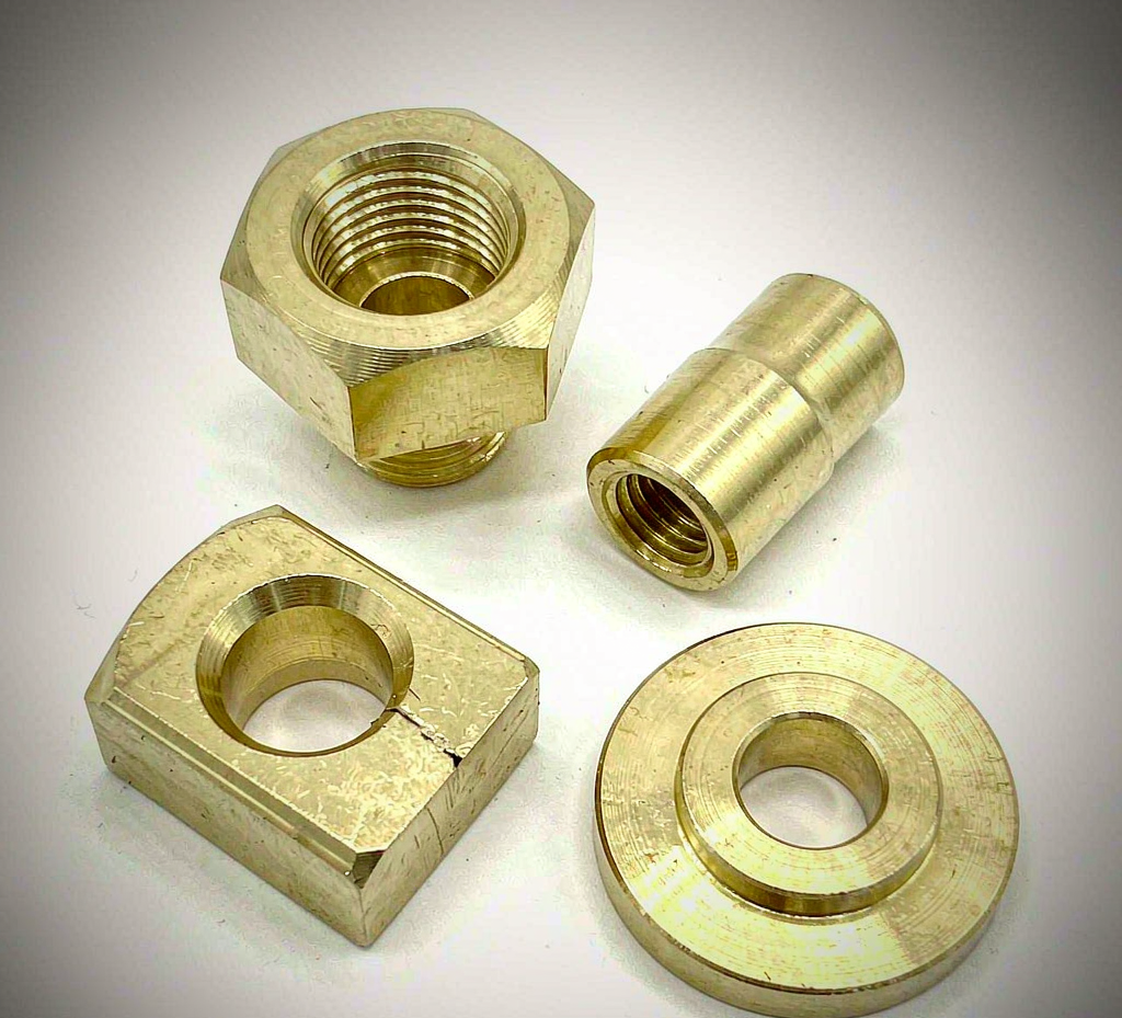 Machined brass CNC components including fittings, connectors and a small housing on a studio background