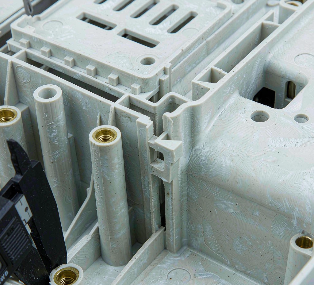 Interior of an injection-molded electronics housing showing PCB mounting bosses with brass threaded inserts, reinforcing ribs and a caliper measuring a boss diameter