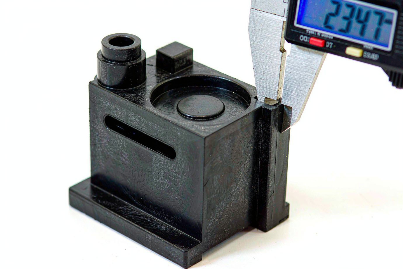 Illustrative — dimensional inspection of a molded black plastic component with a digital caliper on a clean bench