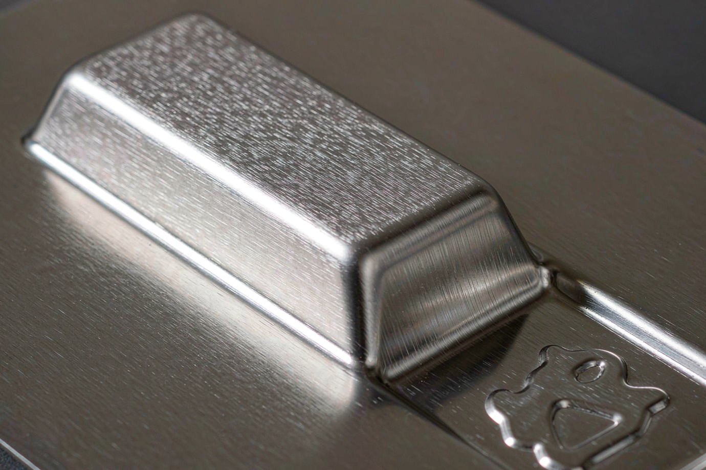 Brushed stainless steel stamped panel showing a raised embossed rib and recessed logo detail