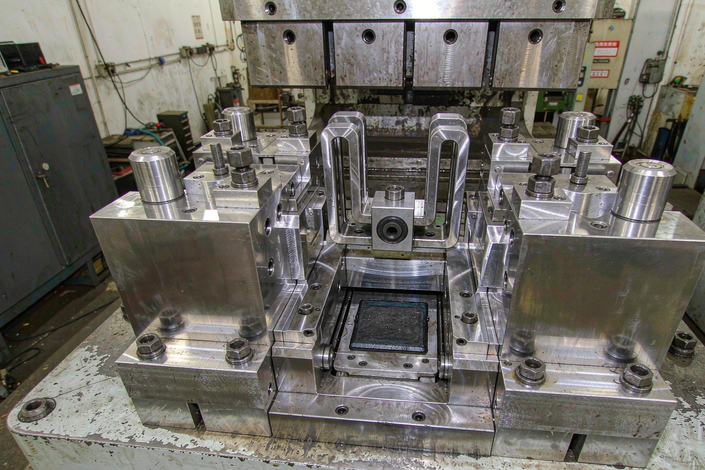 Metal stamping progressive die tooling set mounted on a press bed in a sheet metal workshop