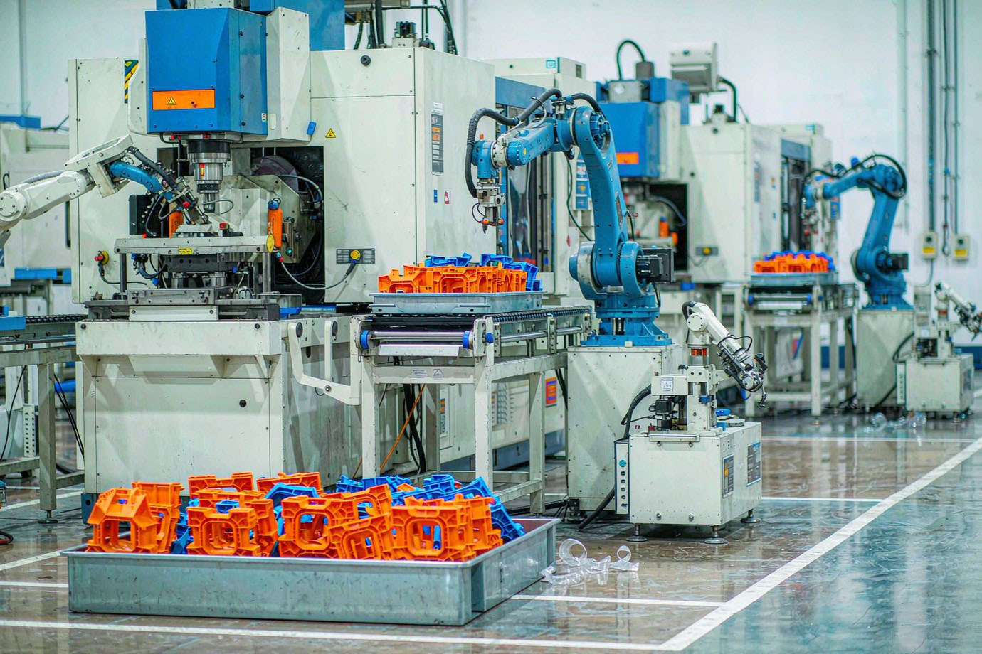 Illustrative — bright modern injection molding machine producing trays of freshly molded strong plastic structural components