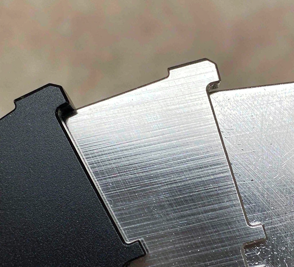 Close-up of machined metal key fob surfaces showing black anodized, brushed stainless and natural aluminum finishes