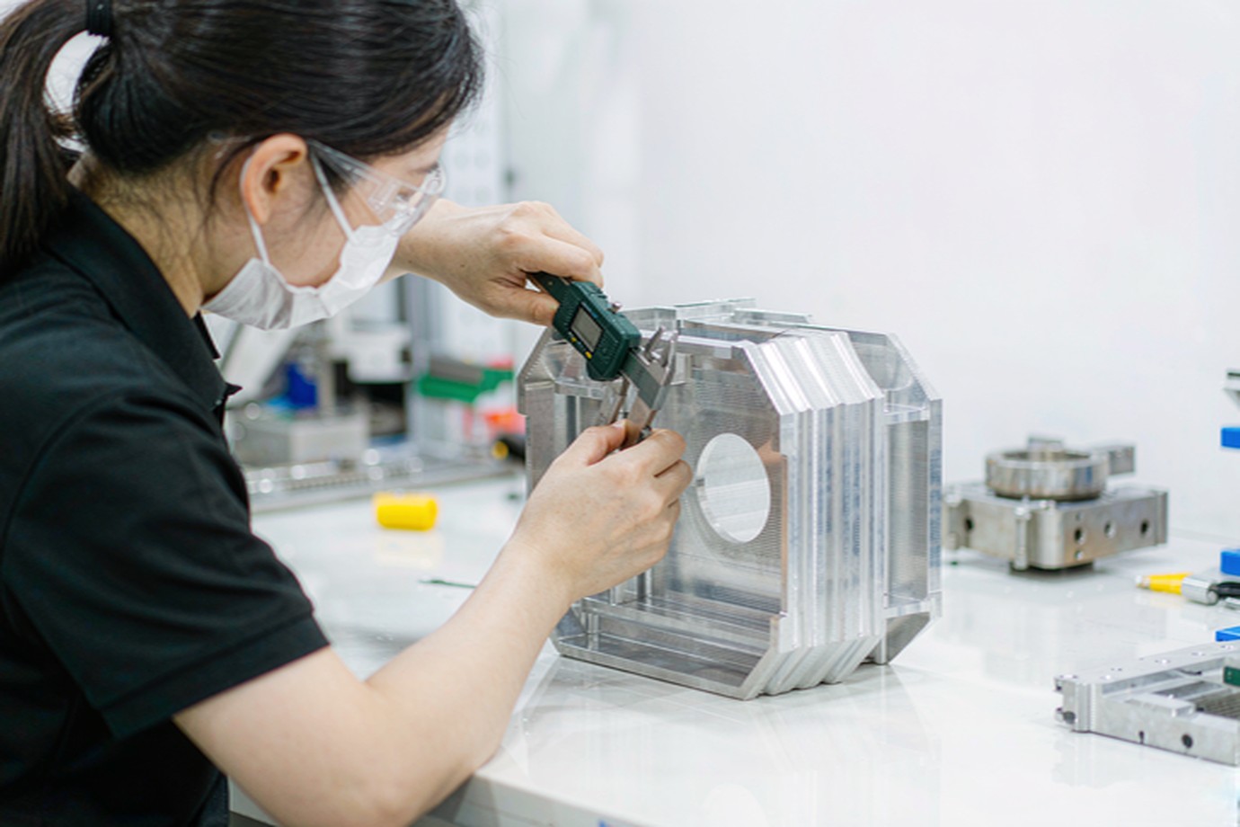 Illustrative — close-up dimensional inspection of a formed sheet metal bracket with a digital caliper on a bright bench