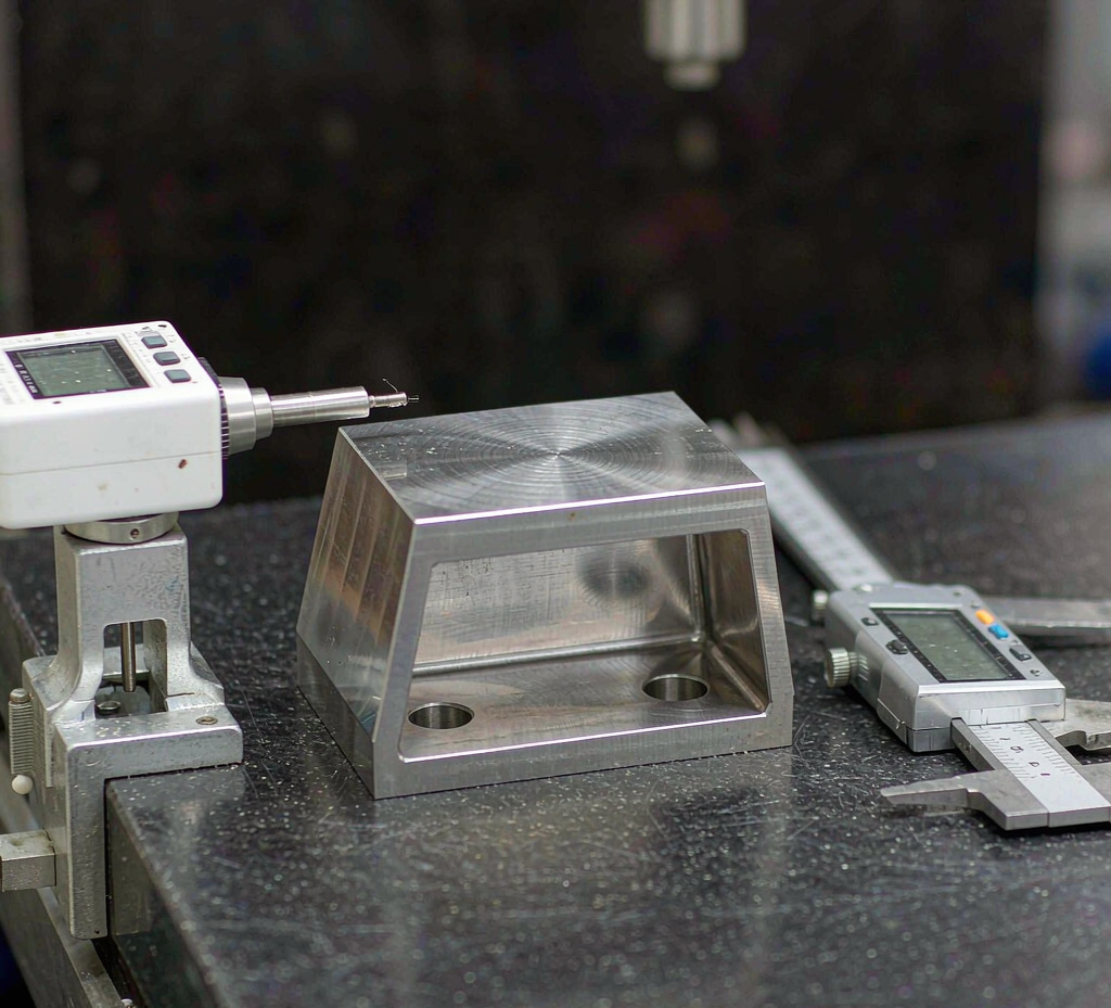 CNC-machined stainless steel bracket being measured for flatness on a granite surface plate with a digital height gauge